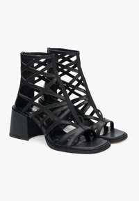 Zwarte open teen sandalen met hak, gekenmerkt door een geometrisch lattice ontwerp van glanzend materiaal en een stevige blokhak.