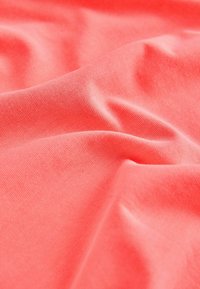 Tissu rose corail doux avec une texture fine tricotée et des plis doux créant une surface lisse et fluide.