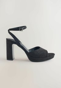 Svart mockaläder högklackad sandal med tjock blockklack, öppen tå och justerbar vristrem med metallspänne. Slät textur.