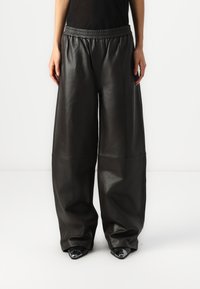Zwarte leren wijde broek met een rekbare tailleband, met slanke verticale naden en zijzakken, gecombineerd met puntige schoen.