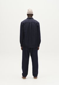 Conjunto de camisa y pantalones de mezclilla azul oscuro con mangas largas, corte relajado y gorro de lana. Diseño simple y textura suave.