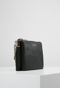 Czarna skórzana torba na ramię o teksturowym wykończeniu, z elementami w złotym kolorze i łańcuszkowym paskiem. Posiada zamek błyskawiczny oraz logo z przodu.