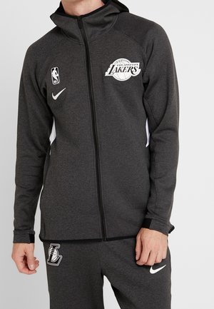 Chaqueta con cremallera negra de Nike con el logo de Los Angeles Lakers, tejido texturizado y paneles laterales blancos; combinada con pantalones negros a juego y un logo de Nike.