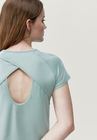 Lichtgroene sporttop met een ronde hals en korte mouwen, met een open achterkant en gekruiste bandjes voor ventilatie.