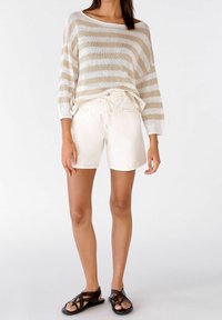 Lichte, crèmekleurige shorts met een tailleband met trekkoord. Gecombineerd met een losgebreide, gestreepte beige en witte trui. Zwarte sandaaltjes met bandjes.