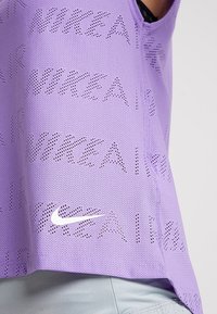 Camiseta deportiva de malla morada con un patrón perforado de "NIKE AIR" y un pequeño logo blanco de Nike en el dobladillo. Diseño ligero y transpirable.