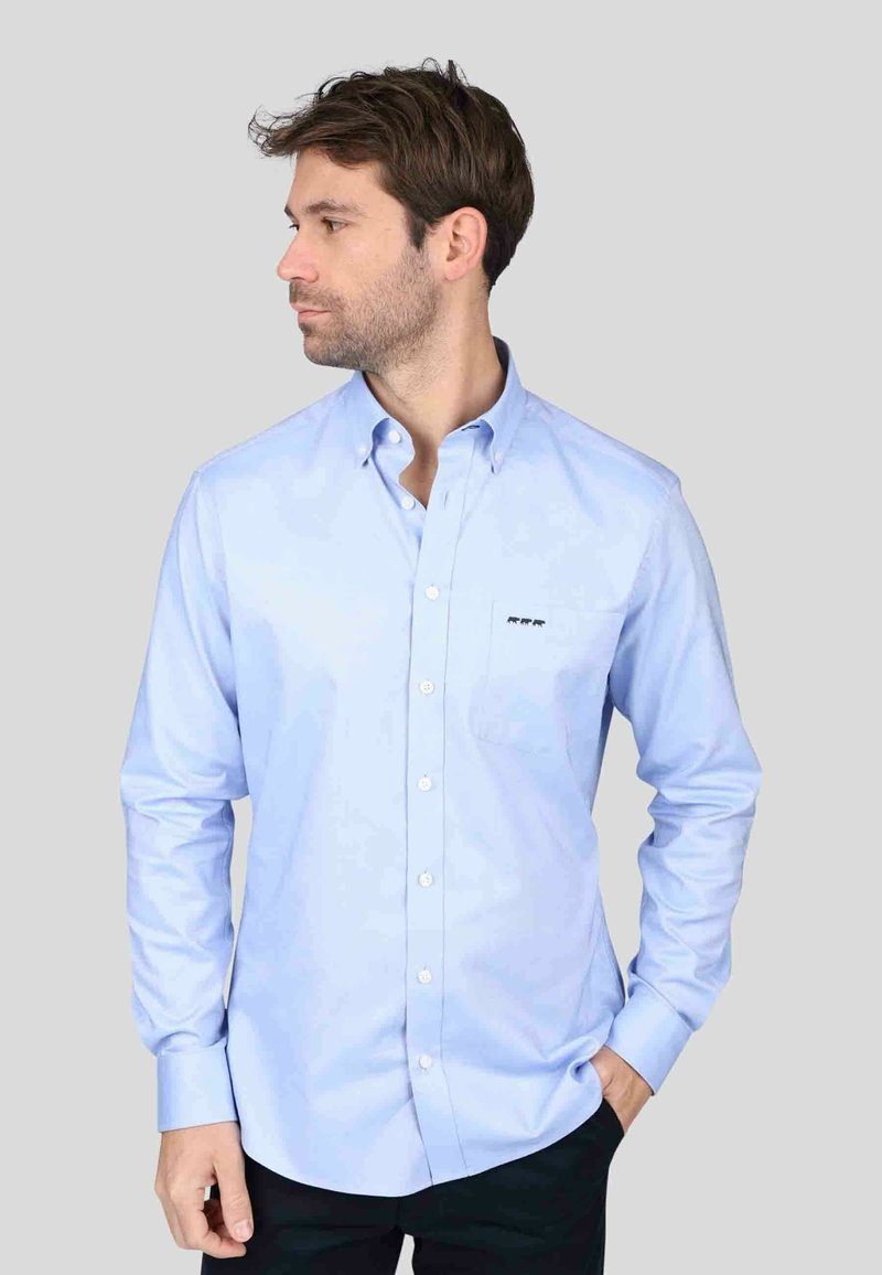 Chemise bleu clair à boutons en tissu lisse, dotée de manches longues, d'une poche poitrine et d'un petit logo brodé sur la poche.