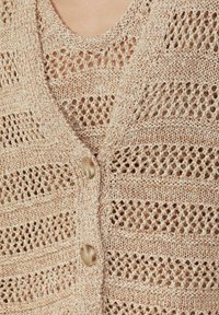 Beige gestrickte Strickjacke mit einem Lochmuster-Design und horizontalen Mustern, großen cremefarbenen Knöpfen und einer strukturierten Oberfläche. Ideal zum Drunterziehen.