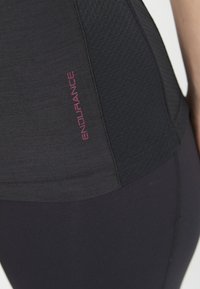 Svart atletisk topp med texturerade sidopaneler och en framträdande rosa "ENDURANCE"-logotyp. Tyget ser slätt och åtsittande ut, perfekt för träningskläder.