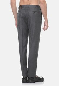 Pantaloni grigi su misura con una texture liscia, dotati di due tasche posteriori, passanti per cintura e una vestibilità dritta. Abbinati a scarpe nere.