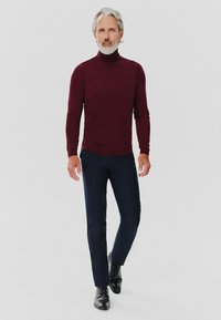 Bordowy sweter z golfem, dopasowany krój, zestawiony z ciemnoniebieskimi spodniami i czarnymi sznurowanymi butami, tworząc elegancki, profesjonalny wygląd.