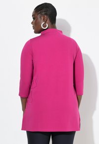 Tunika fucsia con maniche a tre quarti, con ricami floreali sul lato. Il tessuto morbido e le fessure laterali aumentano il comfort e la mobilità.