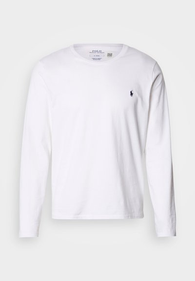 Bílá bavlněná košile s dlouhým rukávem, kulatým výstřihem a malým tmavě modrým logem na levé straně hrudníku. Hladká textura, klasický střih, bez vzorů.