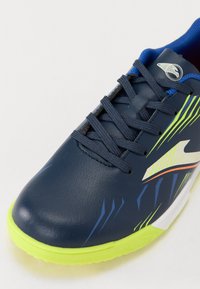 Scarpa sportiva blu navy con un design elegante, caratterizzata da accenti verdi, tomaia in pelle testurizzata e grafica colorata sui lati.