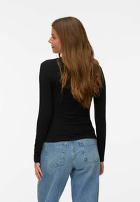 Svart långärmad topp med en figurnära design, tillsammans med ljusblå jeans med hög midja. Slät textur och minimala sömnadsdetaljer.