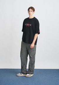 Crni oversized T-shirt s "JORDAN" logotipom u sivoj i crvenoj boji; labave sive cargo hlače s više džepova; bijeli i sivi tenisice.