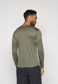 Majica s dolgimi rokavi v olivno zeleni barvi, lahka, teksturirana tkanina, okrogli ovratnik, z rahlo ukrivljenim robom in logotipom na strani.