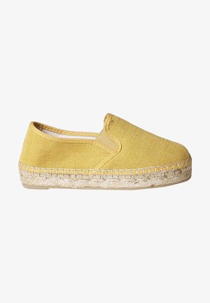 Chaussure slip-on en tissu jaune avec une surface texturée, un bout arrondi et une semelle en jute tressé. Détails de couture le long du bord de la semelle.