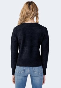 Pulover negru, pufos, cu mâneci lungi, gât rotund și un finisaj texturat. Asortat cu blugi de denim ușor albaștri.