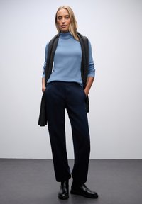 Jasnoniebieski golf z miękkiego materiału. Ciemnoszary szalik luźno zarzucony, granatowe spodnie w dopasowanym kroju, proste nogawki. Czarne botki na kostkę o gładkim wykończeniu.