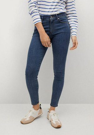 Jeans ajustados de mezclilla de color azul, diseño de talle alto, con un estilo clásico de cinco bolsillos y una textura suave. Usados con zapatillas blancas y beige.