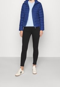 Sininen puffatakki, kevyt, vetoketjukiinnityksellä ja kohotetulla kauluksessa, yhdistettynä vaaleansiniseen t-paitaan ja mustiin skinny-farkkuihin. Valkoiset tennarit vihreillä yksityiskohdilla.