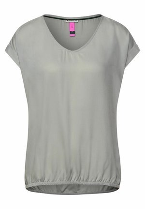 Blouse gris clair à manches courtes avec un col en V arrondi et un ourlet élastiqué, en tissu lisse, présentée sur un fond uni.