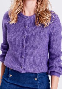 Fialový, pletený kardigan s kulatým výstřihem, pěti kovovými knoflíky a ohrnutými manžetami. Měkká textura s mírně volným střihem.