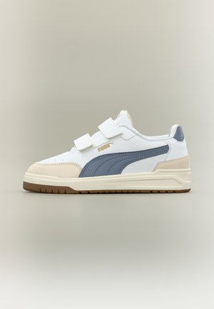 Baskets Puma blanches et beiges avec bande latérale bleue, deux brides velcro et semelle en caoutchouc couleur gomme sur fond clair uni.