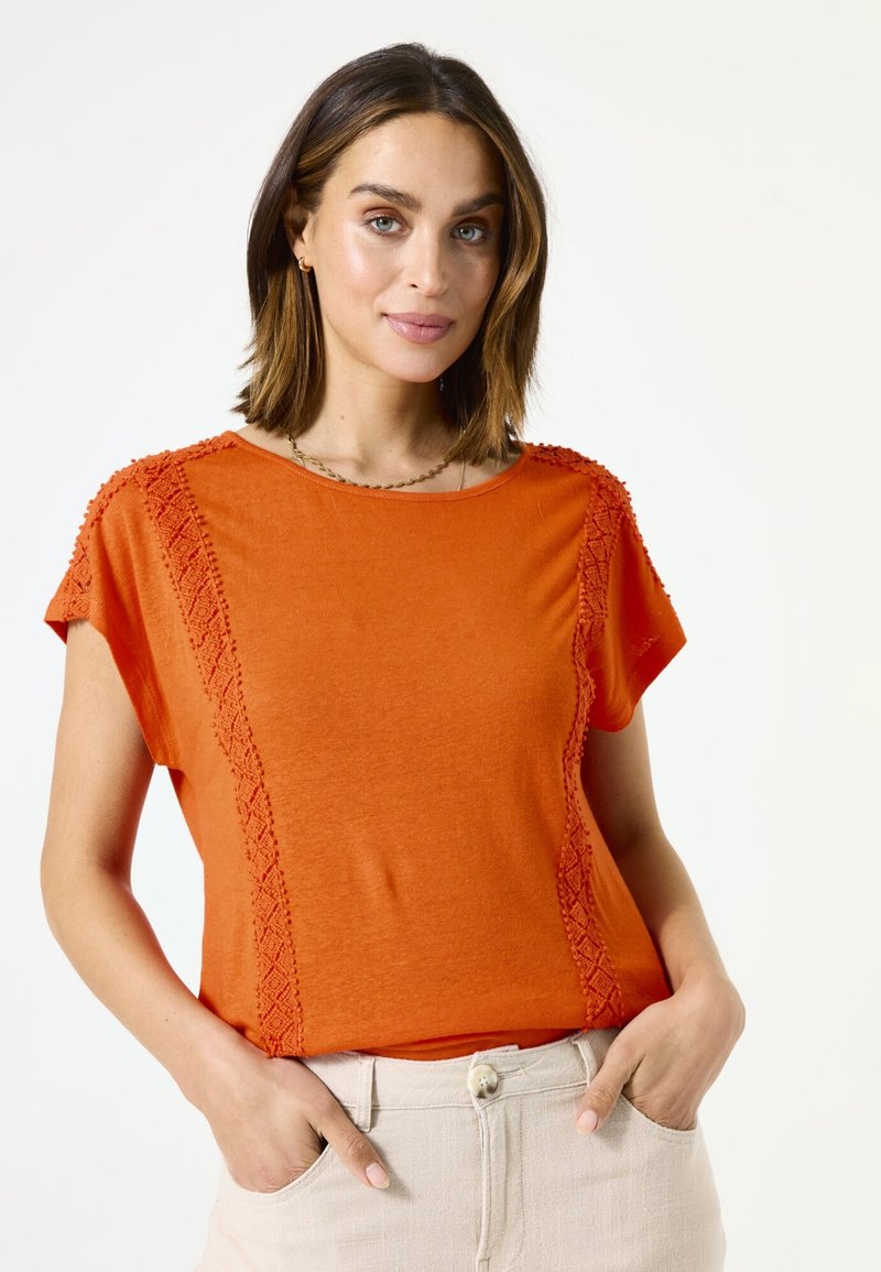 Camiseta de color naranja de manga corta con borde texturizado a lo largo de los hombros y los lados; cuenta con un corte relajado y un diseño de cuello redondo.