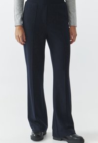 Marine lange broek van een zachte stof, met voorplooien en een hoge taille. Zwarte chunky schoenen maken de outfit compleet.