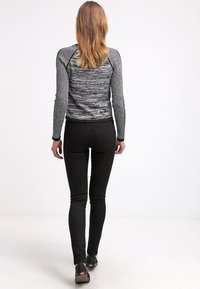 Top de manga larga en negro y gris con un patrón texturizado, combinado con pantalones negros ajustados y zapatos sin cordones. Vista desde atrás.