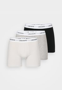 Három pár férfi boxer alsó fehér, szürke és fekete színben. Mindegyik fehér derékgumival rendelkezik, amelyen ismétlődő "Lacoste" logó található. Puha pamut anyag.