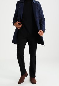 Námořnický trenčkot s dvouřadým zapínáním, černý pletený svetr, černé kalhoty a hnědé semišové kotníkové boty. Hladká textura, tailored střih.