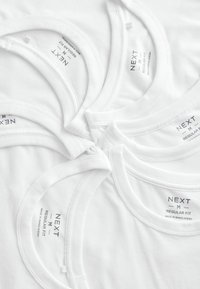 Witte katoenen tanktops gerangschikt in een cirkelpatroon, met een ronde hals, met labels waarop "NEXT M REGULAR FIT" staat en gemaakt in Bangladesh.