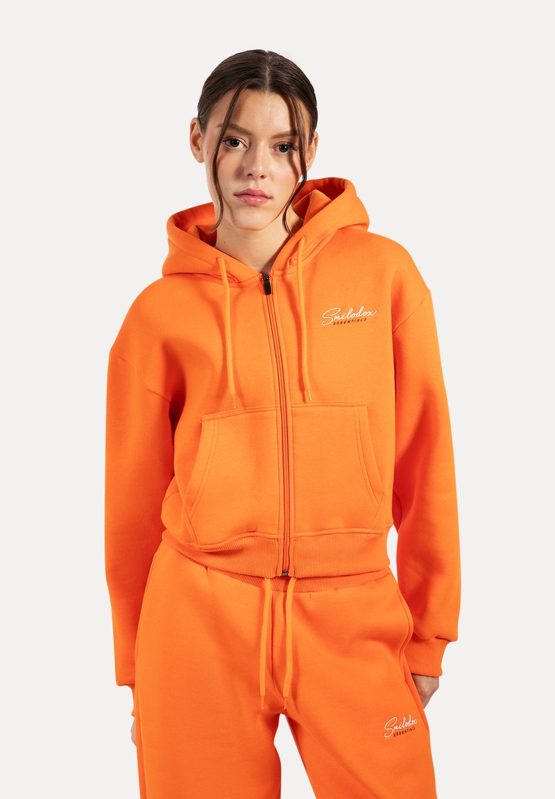 Haut à zip orange en mélange de coton, doté d'une poche avant, de poignets côtelés et d'un logo brodé sur la poitrine. À associer avec un pantalon assorti.
