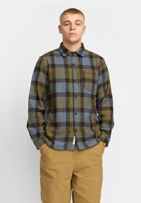 Groene, blauwe en bruine ruitjes flanellen shirt met een knoopsluiting, lange mouwen en een enkele borstzak. Gemaakt van textuurstof.