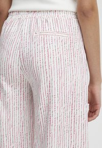 Pantalon blanc avec des rayures verticales rose et bleu clair, accents marron, taille élastique et une poche arrière.