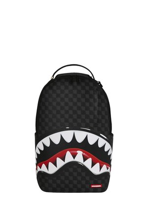 Mochila negra a cuadros con un gráfico audaz de una boca roja y afilados dientes de tiburón blancos en el bolsillo delantero.