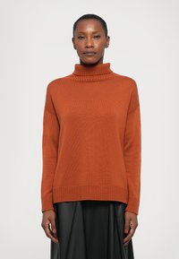 Rustrød turtleneck genser med ribbestrikket kant og mansjettle, laget av teksturert strikket materiale, kombinert med et svart skjørt.