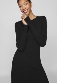 Μαύρο ζιβάγκο φορεμα με ραβδωτή πλέξη, μακριά μανίκια, εφαρμοστή κορυφή και φαρδύ κάτω μέρος. Διαθέτει στρογγυλή λαιμόκοψη και λείο ύφασμα.