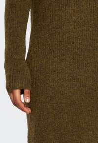 Strickpullover in dunkelolivgrün mit gerippten Bündchen und einer weichen, strukturierten Oberfläche. Verfügt über einen fingerlosen Design an den Bündchen.