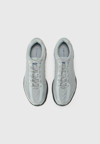 Lichtgrijze sportieve schoenen met mesh-bovenkant, textuurdetails en een zwarte rubberen zool. Heeft vijf gaatjes voor veters en een logo op de tong.
