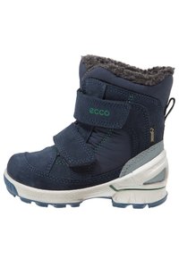 Botín azul oscuro con forro de piel sintética gris, correas de Velcro, parte superior texturizada y una suela deportiva blanca con acentos verdes.