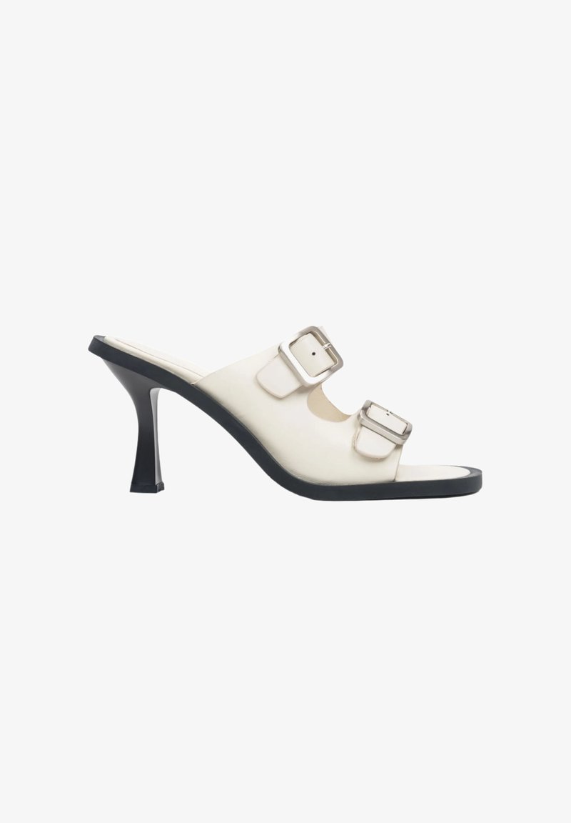 White heeled mules with two adjustable straps and silver buckles. Glossy finish, open toe design, and a black textured sole.