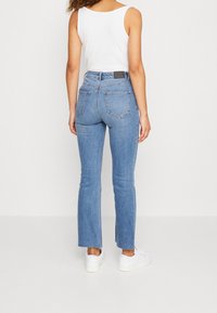 Jeans de mezclilla azul claro con corte recto, que cuentan con dos bolsillos traseros y una cintura de altura media. Combinados con zapatillas blancas.