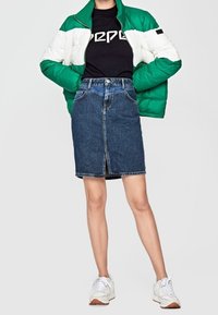 Grön och vit puffjacka, svart T-shirt med vitt logotyp, denimkjol och vita sneakers. Avslappnad outfit med tydlig färgkontrast.