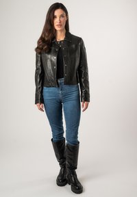 Zwarte leren cropped jack met drukknoopsluitingen, voorzakken en een kraag, gecombineerd met blauwe jeans en hoog zwarte laarzen tot de knie.