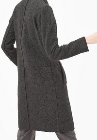 Long charcoal gray coat made of textured fabric. Features a lapel collar, long sleeves, and side pockets. Clean, tailored silhouette.