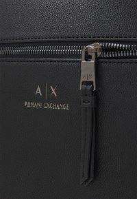 Borsa nera in pelle testurizzata con zip e hardware metallico argentato. Presenta il logo impresso "A|X ARMANI EXCHANGE" sopra il tirante della zip.